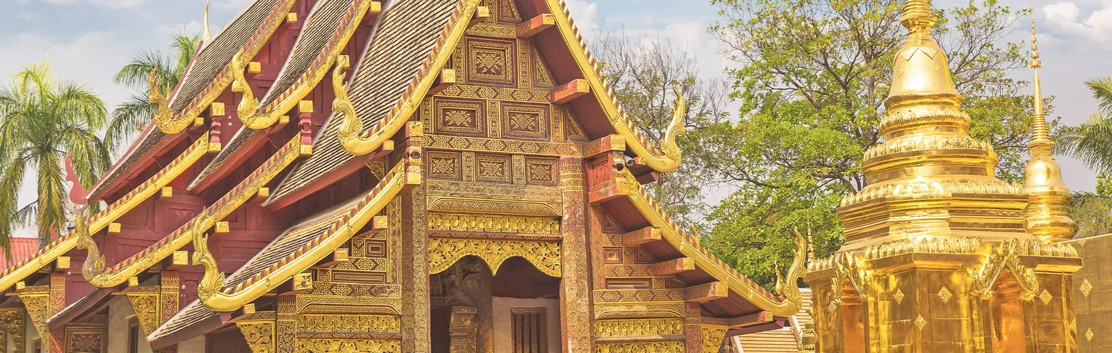 Templo tailandês ornamentado e monumento dourado cercado por jardins.