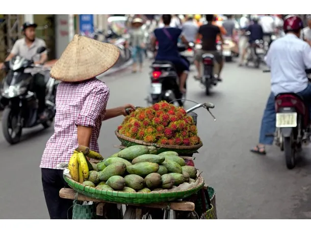 Feirante organiza frutas frescas em uma banca de mercado tailandês.